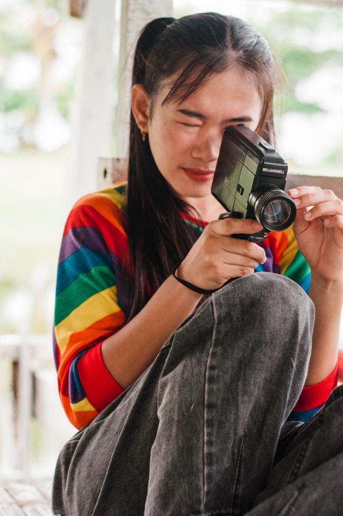 Portrait of a young woman in a rainbow shirt using a vintage camera outdoors.