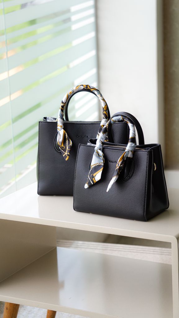 Stylish black leather handbag with decorative handles on a minimalist shelf.